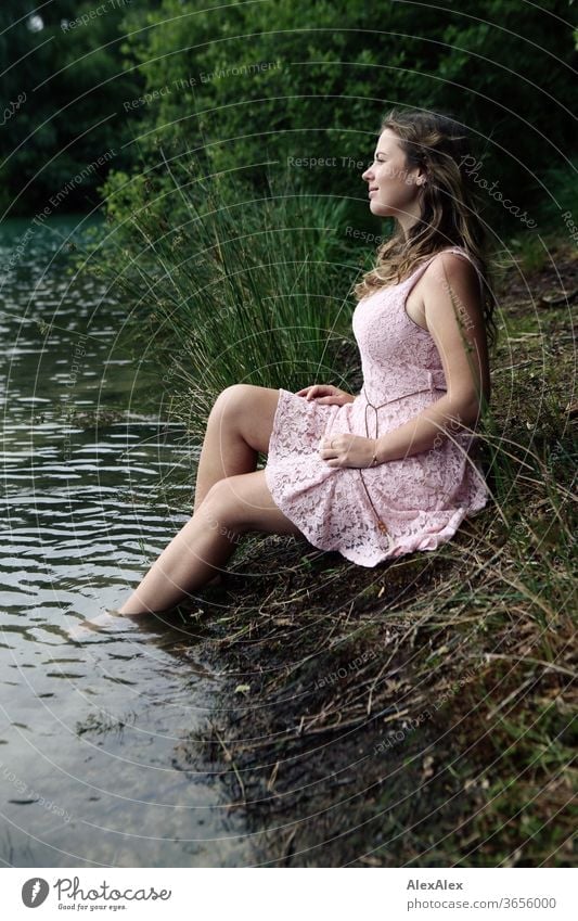 Young woman in a pink summer dress sitting in a clearing with her feet in the forest lake Woman girl Forest Grass plants foliage green Nature Dress Barefoot