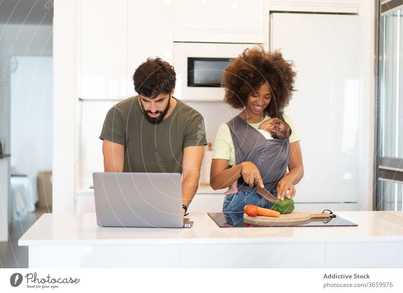 Multiracial family together in kitchen counter parent cook work father mother baby multiethnic multiracial diverse african american black arab laptop love child