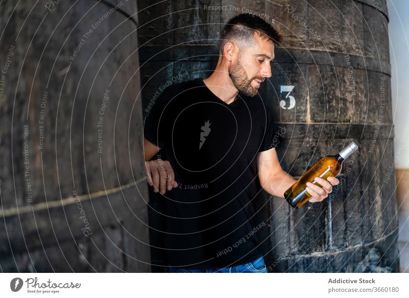 Winemaker with bottle of wine near huge wooden barrel winemaker check positive winery factory viticulture winemaking production industry contemporary