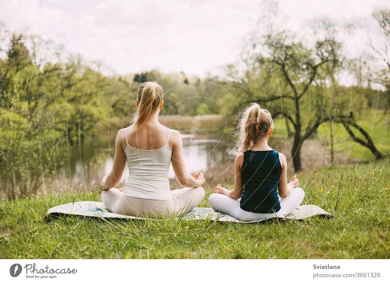 Mother and daughter sit in the Lotus position in the garden. The family practices yoga outdoors. Back view, space for text meditation lotus together mum