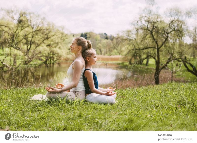A beautiful young woman and a fair-haired girl are meditating in the Lotus position. Family vacation, meditation. Side view, space for text yoga outdoor lotus