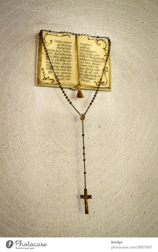 A rosary hangs from an open Christian prayer book with the Our Father - prayer Rosary Lord's Prayer Bible Christianity Religion and Faith Catholicism