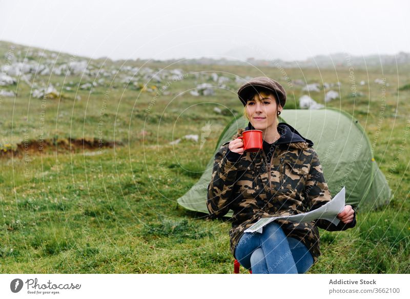 Focused woman with map sitting near camping tent in nature navigate adventure concentrate focus location traveler wanderlust freedom landscape joy casual
