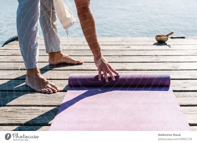 Man with yoga mat on pier on sunny day man singing bowl meditate wooden embankment sea healthy practice harmony relax male casual barefoot balance wellness