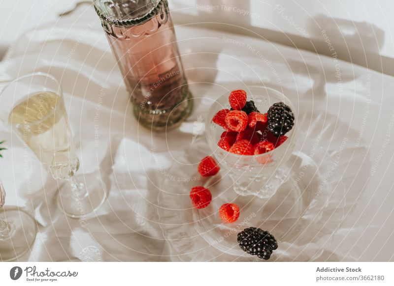 Glass of cocktail with berries and glasses served on table against white wall bottle plate berry drink composition decoration design creative elegant style