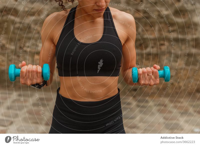 Fit ethnic sportswoman training with dumbbells on embankment during workout squat balance reached arm pavement stretch practice flexible activewear strong
