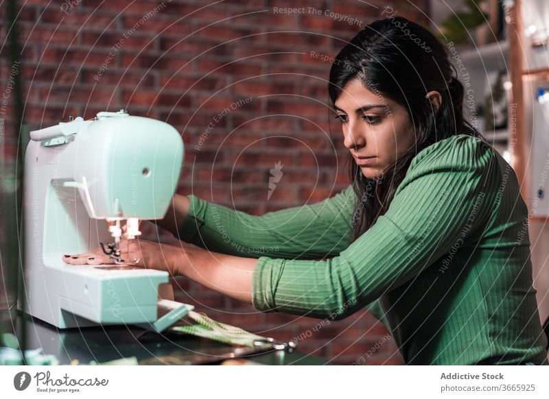 tailor sewing on machine near brick wall in atelier sewing machine handicraft sample pattern lamp small business workshop fabric artisan using equipment process