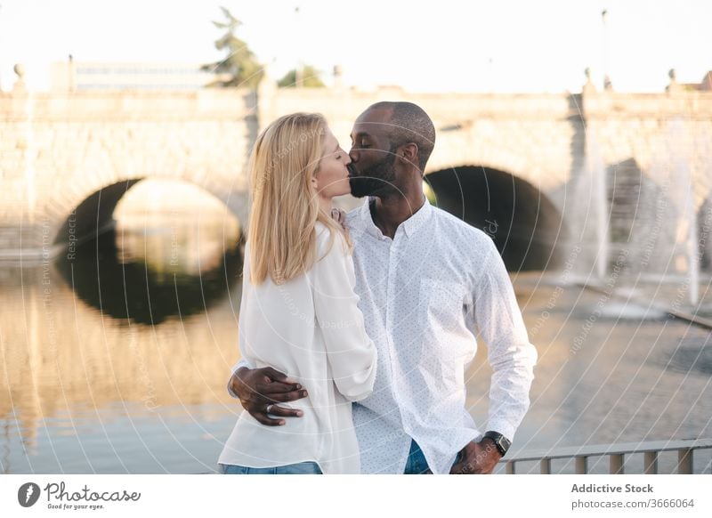 Loving ethnic couple kissing in sunny park - a Royalty Free Stock