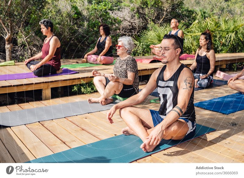 Multiethnic people practicing yoga during summer vacation meditate lotus pose padmasana practice tropical resort relax harmony wellness healthy eyes closed