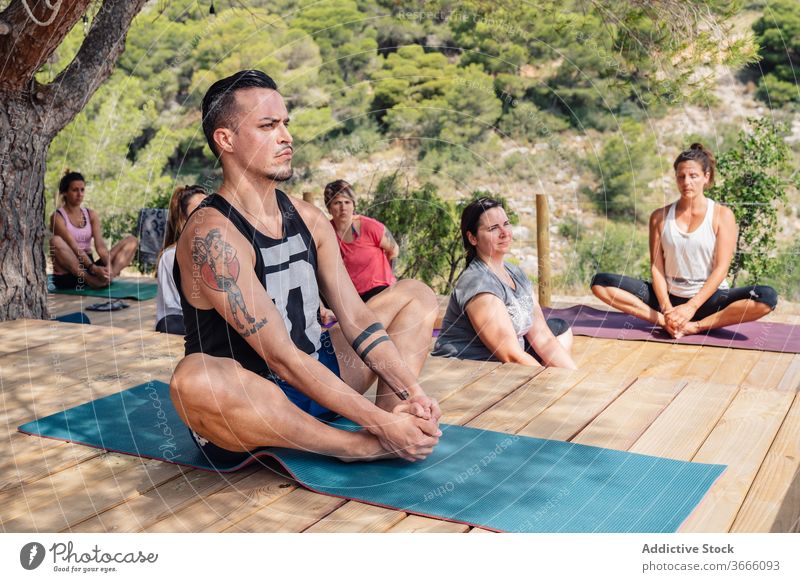 Group of multiethnic people stretching legs while practicing Butterfly yoga asana butterfly baddha konasana class camp park concentrate wellness practice