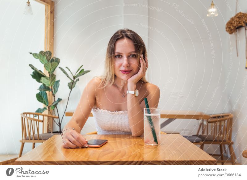 Smiling young woman sitting at table in cafe rest drink looking at camera positive female top casual relax beverage leisure lady blondie cheerful chill enjoy