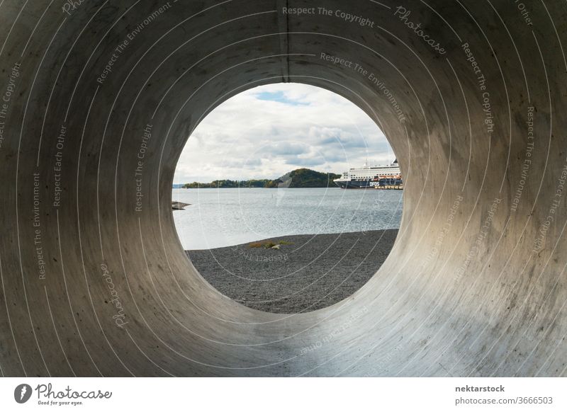 View through concrete pipe to beach and water with cloudscape Oslo Norwegian Norway capital city urban outside outdoors day tunnel view through cylindrical