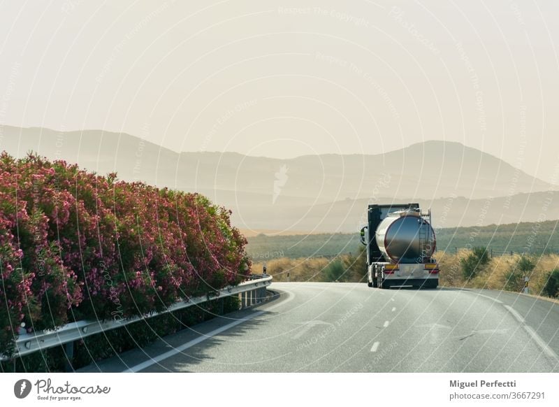 Tanker truck driving on the highway with a background of mountains at sunrise tank truck road travel landscape nature liquid transport mist transportation