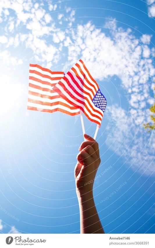 Hand holding two american flags on the blue sky with sunlight background, waving flag for United States of America close-up national patriotism red freedom usa