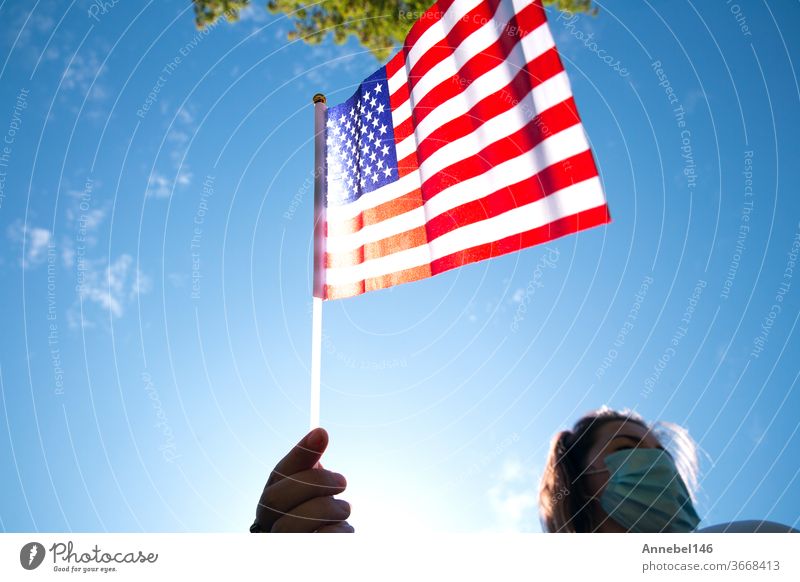 Young woman holding American flag on blue sky with sunlight and safety mask for Covid-19 waving for Usa america usa patriotism outdoors girl freedom patriotic