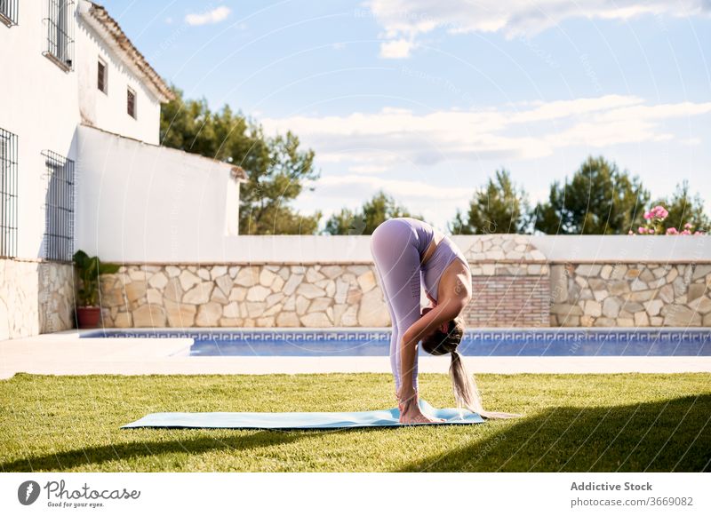 Woman doing yoga in Uttanasana on terrace forward bend practice woman uttanasana flexible pose lawn female sportswear mat healthy exercise stretch wellness
