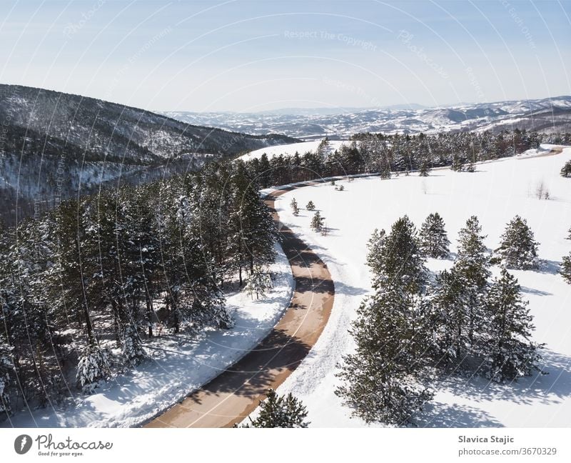 Winter landscape in sunlight. View on the mountain road surrounded by evergreen trees in winter, drone shot above aerial asphalt background cabin cold