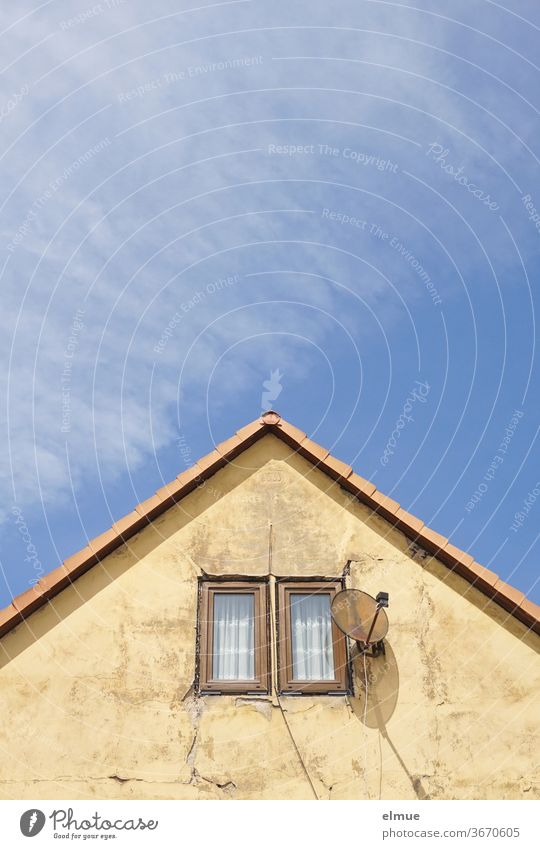 cracked older gable wall with two small windows and a satellite dish with shadow in front of a blue sky with fair weather clouds peak Window Satellite Dish