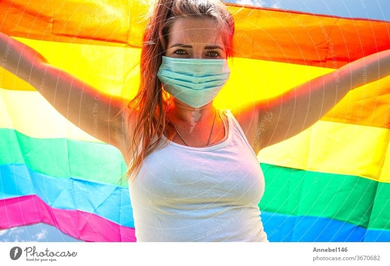 Young woman waving a rainbow flag for LGBT rights, freedom for homosexual Lgbtq concept, wearing a safety mask for Covid-19, coronavirus. Protesting lesbian