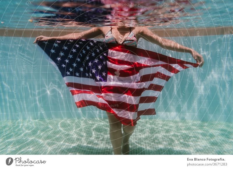 young woman in a pool holding american flag underwater. 4th july independence day concept. Summertime swimming pool summer sunglasses caucasian fun beautiful