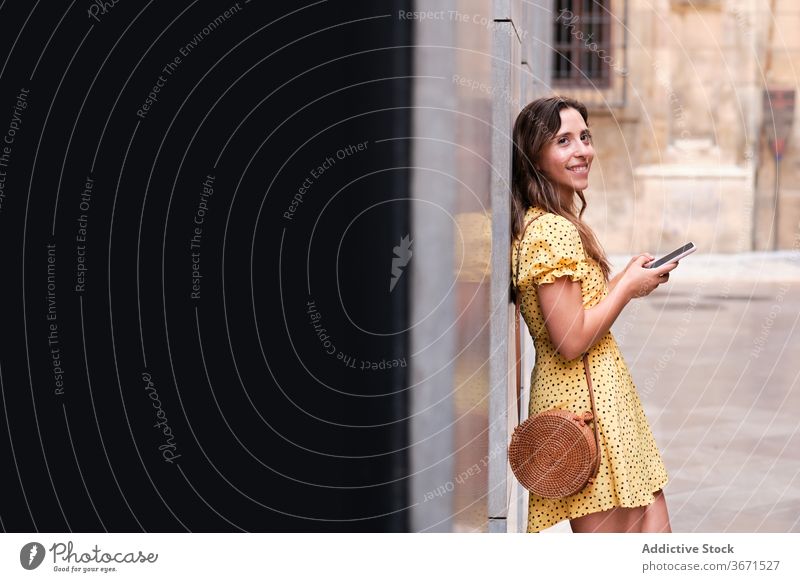 Cheerful woman using smartphone in city stroll summer building urban smile browsing female dress cheerful mobile phone online lean surfing device gadget lady