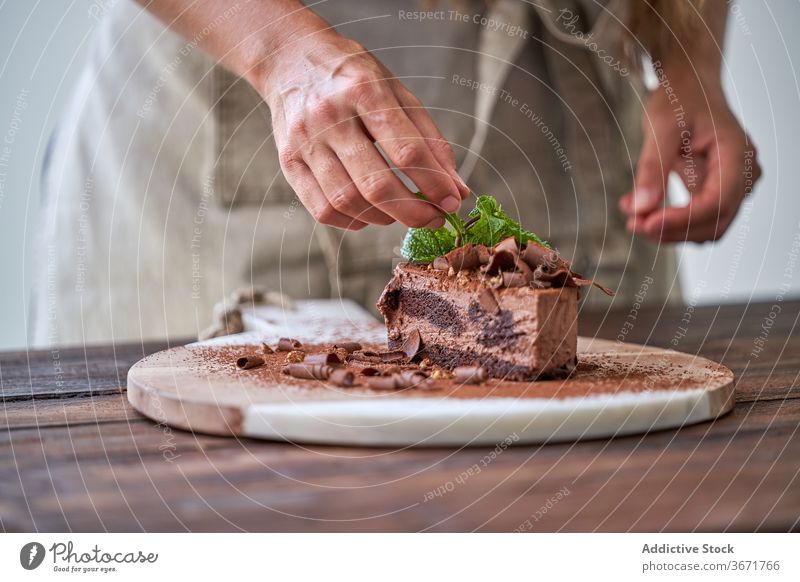 Chef garnishing chocolate cake with mint confectionery woman mousse decorate make dessert kitchen half cut baked cream female cook food sweet candy homemade