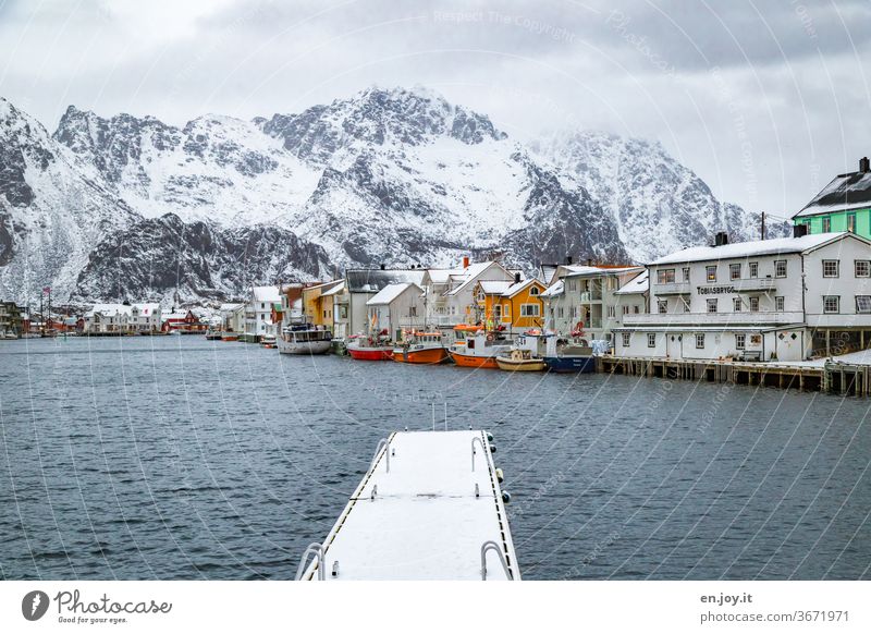 Nordic small town on the fjord with fishing boats and jetty in front of snowy mountains Henningsvær Lofotes Norway Fishing village Footbridge landing stage Snow