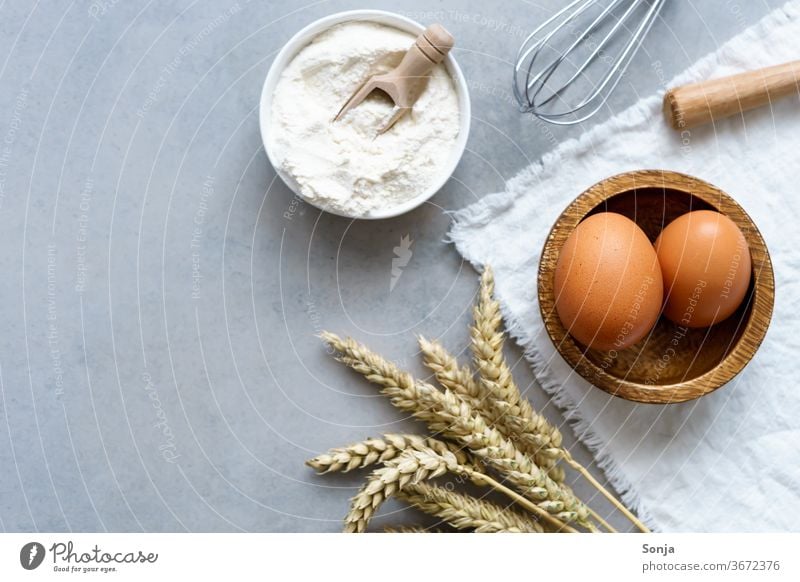 Ingredients for cakes and biscuits on a grey kitchen table. Wheat ear, brown eggs and flour, top view Flour Preparation Dough Bread Baking Raw Baked goods