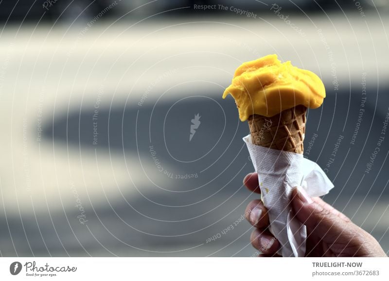 https://www.photocase.com/photos/3672683-if-the-weather-is-nice-and-hot-all-children-want-ice-cream-mango-mango-schleck-schleck-a-womans-hand-holding-an-ice-cream-cone-with-a-ball-of-yellow-mango-ice-cream-with-a-paper-napkin-in-front-of-light-and-shadow-on-the-street-photocase-stock-photo-large.jpeg