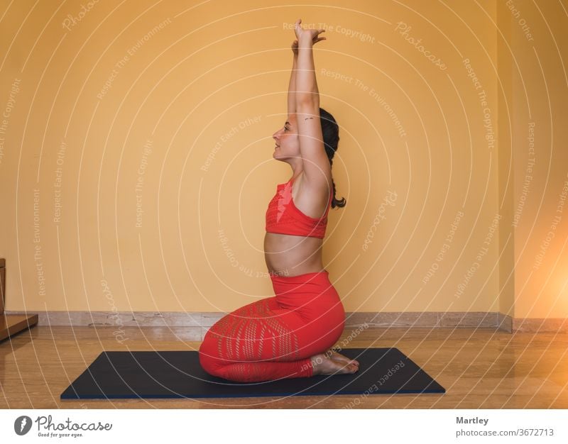 Fit young girl doing yoga at home by covid confinement. Young woman in sportswear stretching her arms while sitting on her legs on the mat in the cozy living room at home.