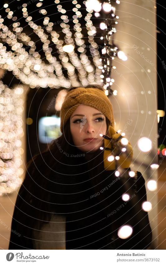 Night portrait of a young woman looking into the distance , leaning on a string of christmas lights. Cold winter night smile bokeh girl beautiful female evening