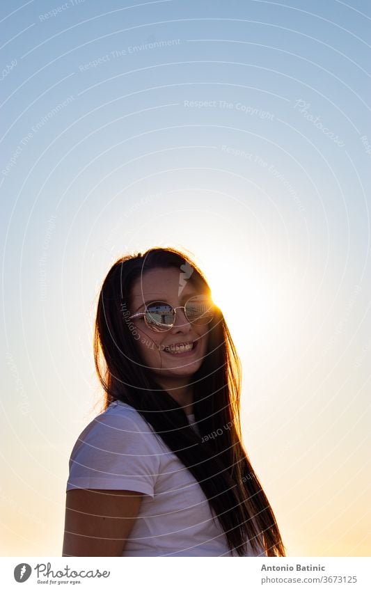 Attractive brunette with sunglasses laughing , sun directly behind her head peeking, golden sunset hour. attractive background beautiful beauty casual caucasian