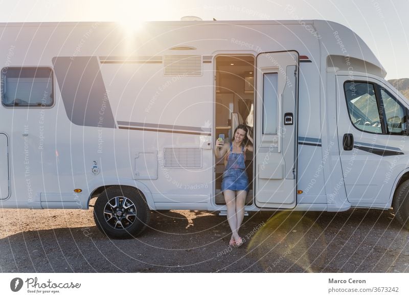 Smiling Young woman taking a selfie on her motor home parked on the beach on a sunny day smiling lifestyles young van desert exploration journey camper van