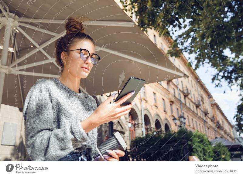 Young stylish pretty woman with smartphone at the outdoor cafe. young city internet public eyeglasses outdoors portrait casual style lifestyle female girl
