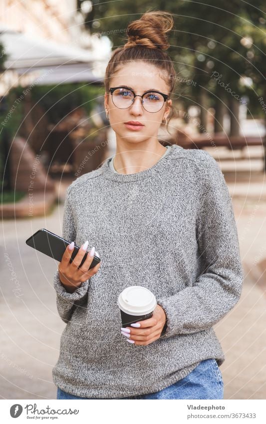 Young girl dressed in casual clothes with smartphone and a cup of takeaway coffee. Daily life of youth. People online woman young city internet public