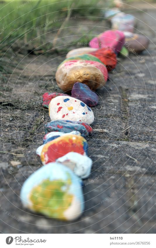 Row of brightly painted lucky stones laid out on the pavement Stone Lucky Stones Painted variegated in rows Good luck charm little artworks Nature trend ideas