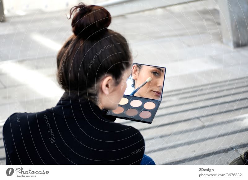 Rear view of a young woman with ponytail sitting on steps outdoors while using a makeup brush day make-up adult one person beauty lifestyle photography applying