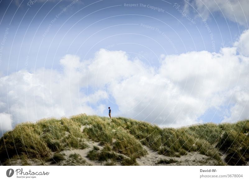 Man stands alone in the dunes and enjoys the peace and quiet Stand To enjoy tranquillity Lonely gap vacation Clouds Small huge landscaping landscape photograph