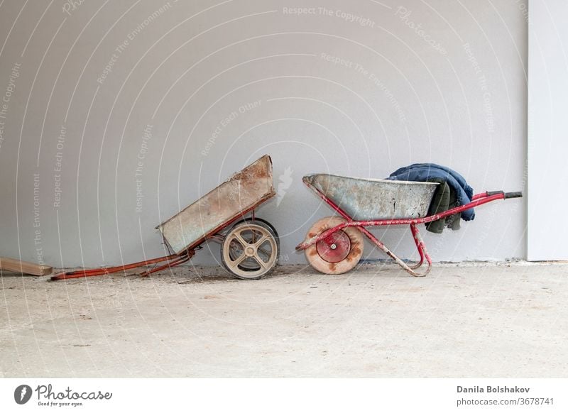 old construction cart and wheelbarrow on the background of a stucco wall construction trolley container retro single wheel vintage gardening metal industry