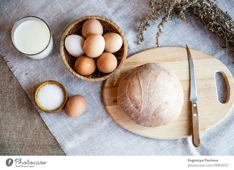 A loaf of fresh homemade bread, milk, eggs and salt on a wooden plate. Still life in rustic style, view from above. Baking Dough biscuits Appetizer background