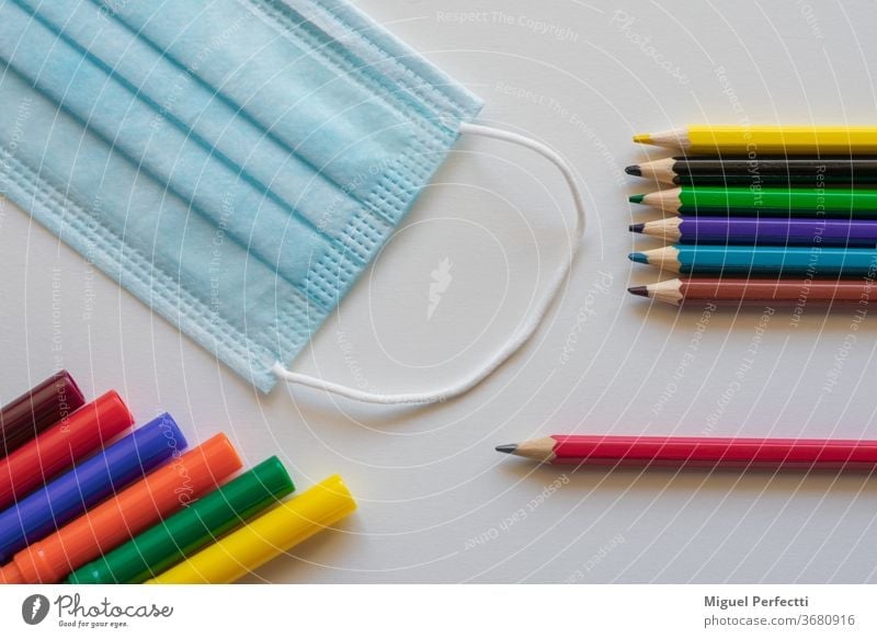 Markers and coloured pencils next to a mask, which are mandatory in many countries to prevent Covid 19 infections in schools back to school Markings crayons