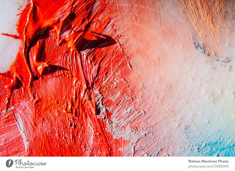 Close-up of a color palette of a painter. Red, orange, white and blue colors. A closeup shot of the red paint mixed up with white paint on the canvas.