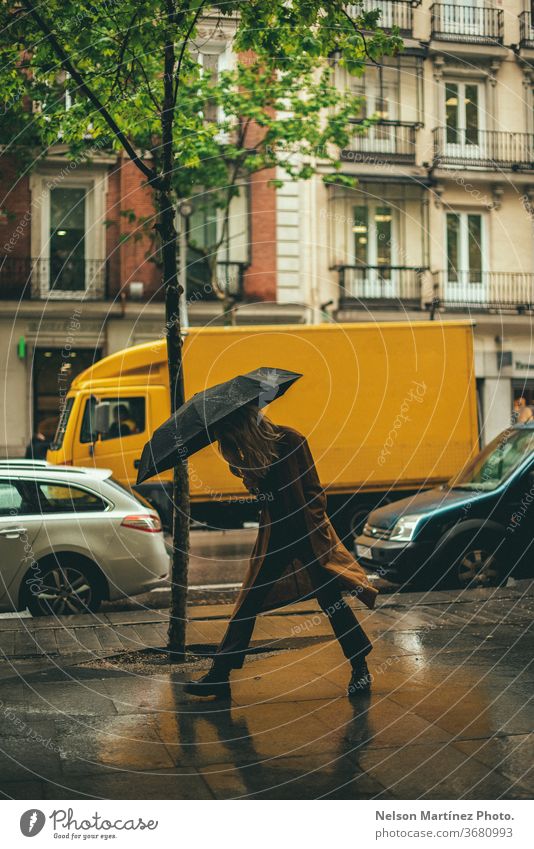 Stylish blonde woman walking in the rain. She is holding a black umbrella in an unban area. rainny Rain Umbrella Weather Wet Human being Bad weather Water