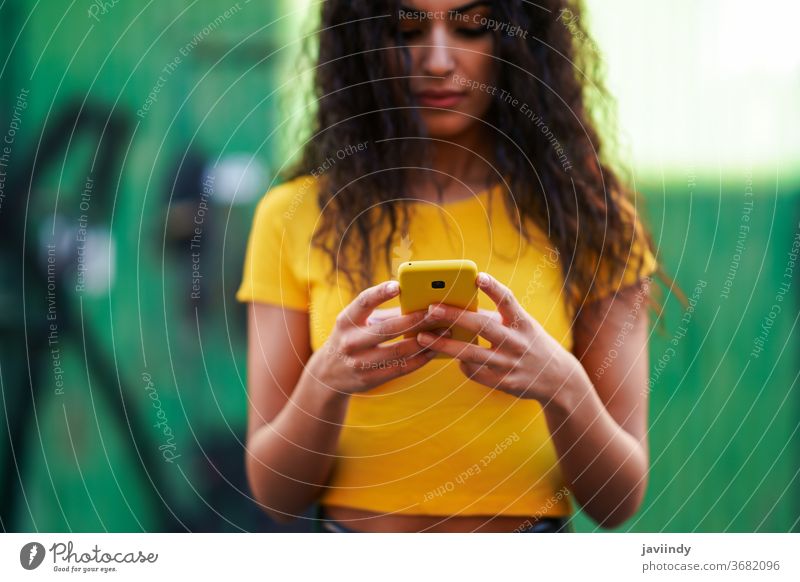 Young Arab woman walking in the street using her smartphone arab young texting message close-up typing yellow copyspace girl recording hairstyle attractive