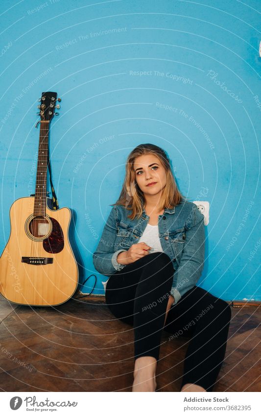 Pensive woman sitting near guitar on floor play thoughtful musician wall acoustic young female casual instrument song melody think pensive sound happy hobby