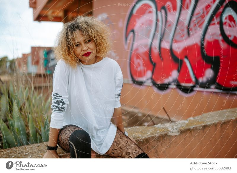 Provocative female millennial on street provocative woman graffiti city urban trendy unemotional creative hairstyle ethnic black african american stone