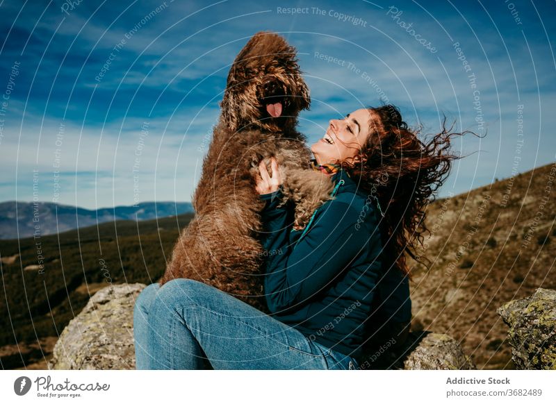 Happy woman playing with dog in mountains laugh travel countryside owner puerto de la morcuera spain female pet labradoodle sky cloudy relax vacation happy