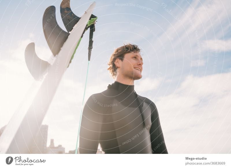 Surfer standing at the beach next to his surfboard. man water sport surfing sea surfer ocean outdoors athletic coastline waves background adventure sports