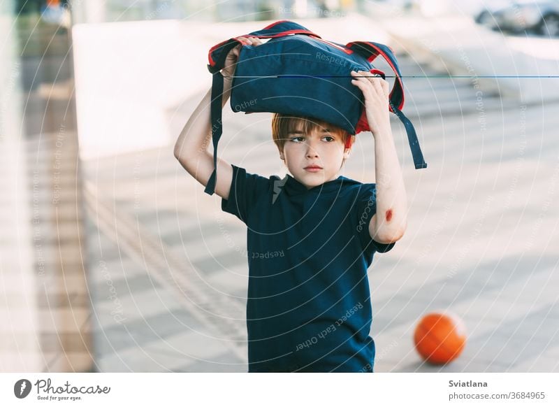 A tired boy in sports uniform and with a wound on his arm returns home after basketball training. Education, upbringing, physical education backpack smile