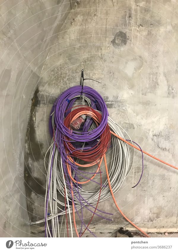 Colorful cables hang rolled up on a concrete wall. Cable tangle Construction site Terminal connector Cables Roll purple variegated Wall (building) Technology